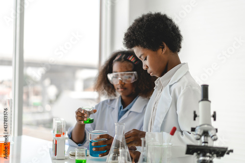 Two african american cute little boy and girl student child learning research and doing a chemical experiment while making analyzing and mixing liquid in test tube at science class in school