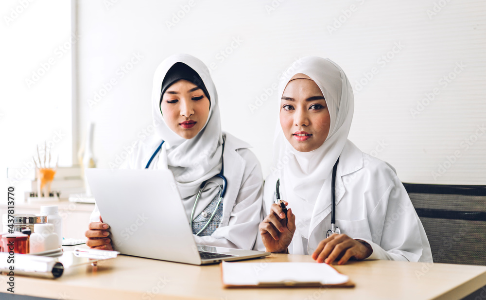 Professional medical two muslim asian woman doctor team with stethoscope in uniform working with laptop computer on desk in hospital.healthcare and medicine Professional medical two muslim asian woman doctor team with stethoscope in uniform working with laptop computer on desk in hospital.healthcare and medicine