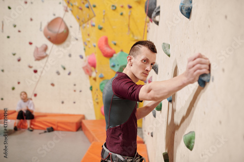 Young sportsman climbing wall in equipped room at leisure center