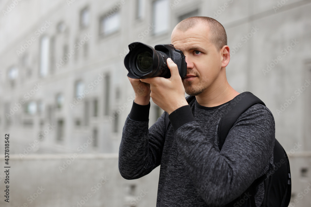male photographer taking photo with modern dslr camera over concrete building background