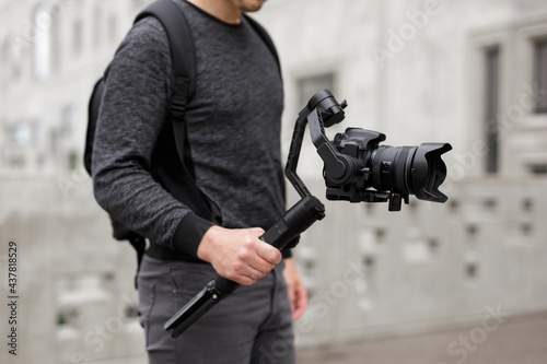 videography, filmmaking and creativity concept - close up of modern dslr camera on 3-axis gimbal stabilizer in male hands over concrete building photo