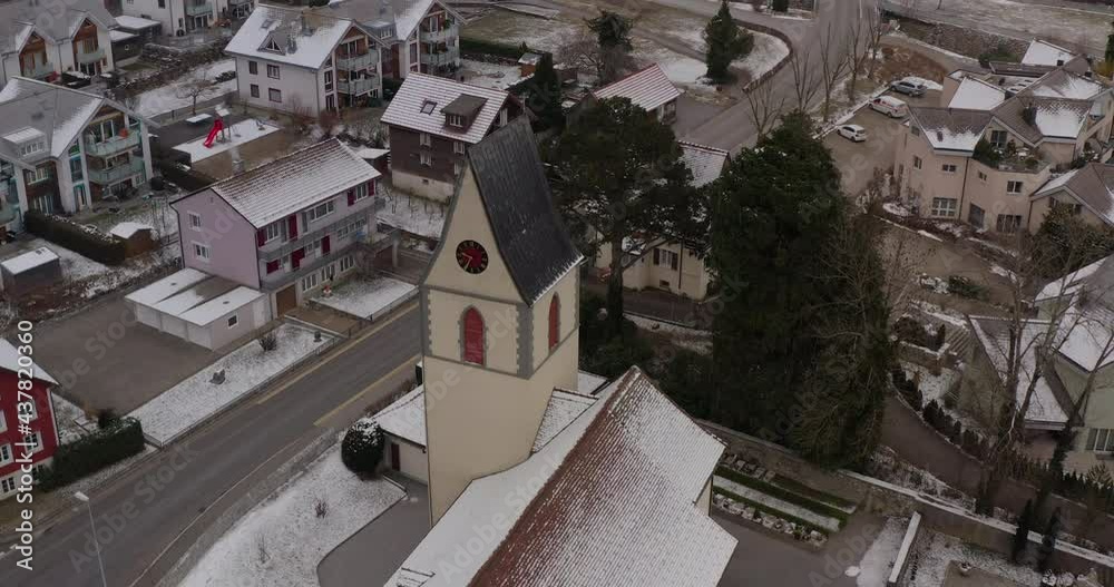 High tower of a christian church in a quite village near Lake Walensee in Switserland on a cold winter day when snow is falling down. Drone dolly shot