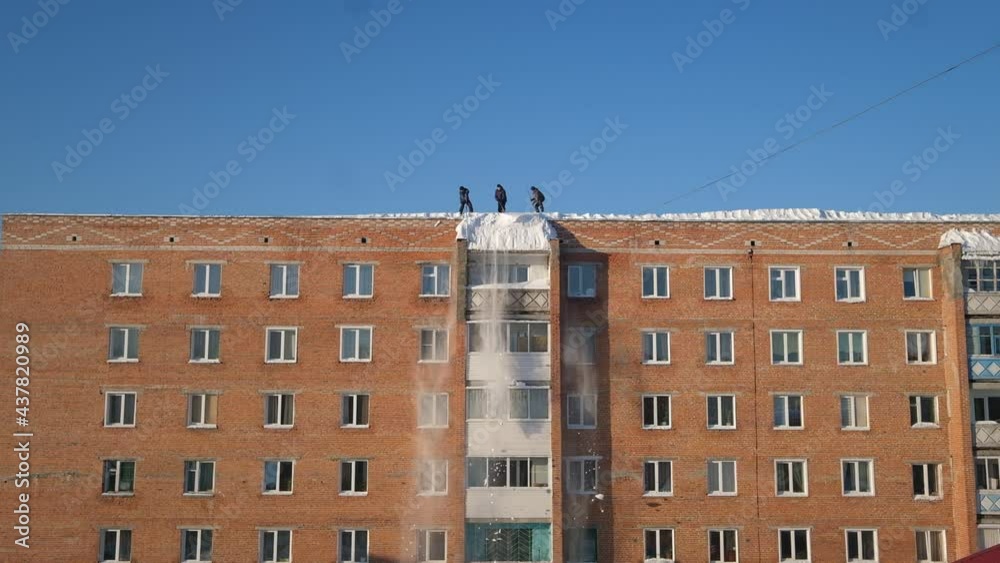 Workers standing on the roof of a residential multi-storey Siberian building cleaning snow on a winter sunny day Workers standing on the roof of a residential multi-storey Siberian building cleaning snow on a winter sunny day