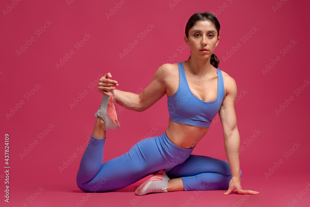 Young woman doing stretching workout on maroon background