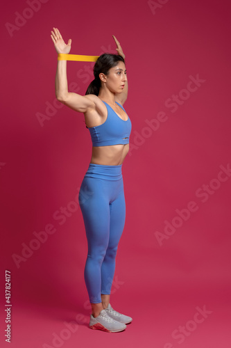 Girl exercising with resistance band loop on maroon background