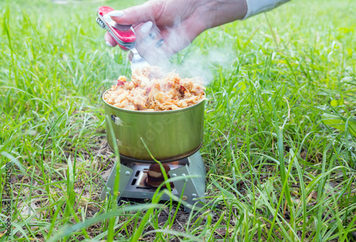 Reheating canned meat on a tourist stove with dry fuel on a camping trip, hiking food concept. photo
