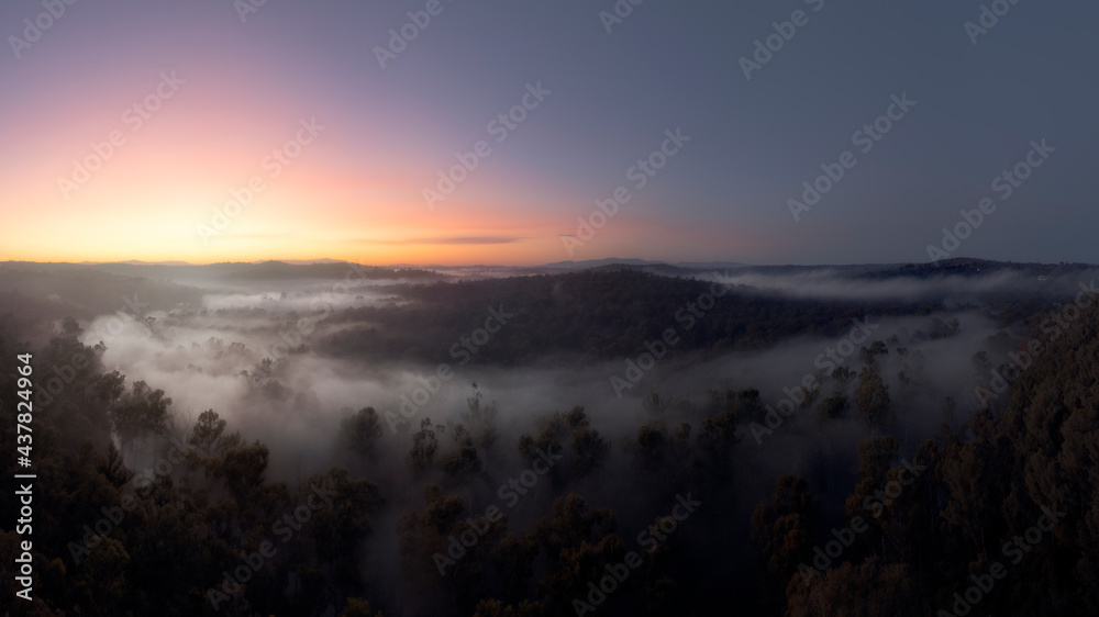 Panoramic aerial view at dawn of Australian countryside with woodlands, fog, hills and sunrise