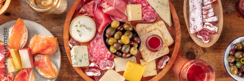 Charcuterie and cheese platter panorama with wine and salmon sandwiches, top shot on a rustic background. A panoramic banner for an Italian antipasti restaurant menu
