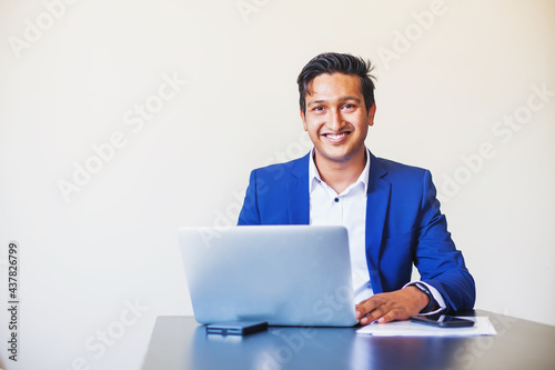 Handsome young professional Indian man in formal suit using laptop in the office over white background
