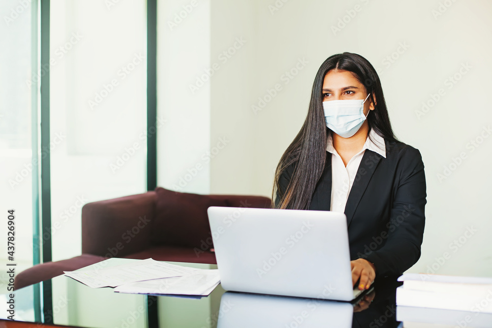 Beautiful Indian woman in face mask working on laptop during coronavirus outbreak Beautiful Indian woman in face mask working on laptop during coronavirus outbreak