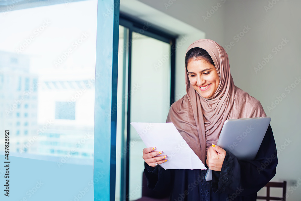 Beautiful arabic Muslim young woman in hijab holding laptop in a city - obrazy, fototapety, plakaty 