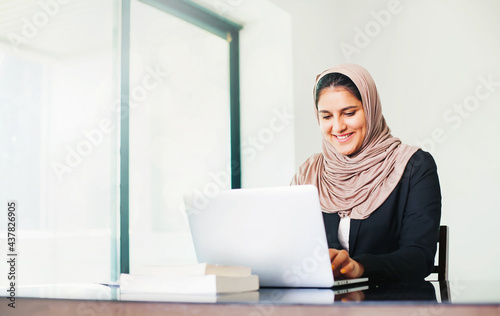 Beautiful fair skinned muslim woman in hijab working in the light office room