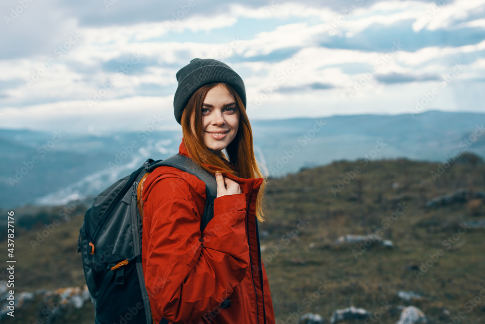 Naklejka premium happy woman in a red jacket with a backpack and in a hat mountains in the background fresh air