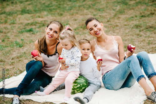 Happy family is eating grapes, apples, watermelon in the park on holidays. Boy, girls with mothers on a blanket on a picnic in the summer.