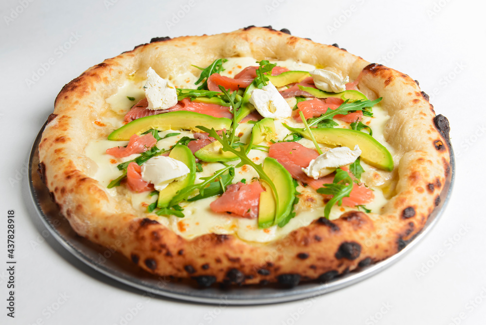 Delicious pizza with salmon, cheese, avocado and fresh arugula. Over white background.