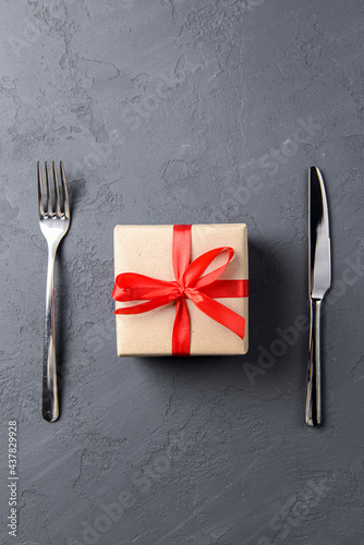 Gift box with red bow over black background with cutlery. Black knife and fork.