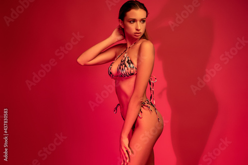 Girl in summer bikini posing on crimson background in studio