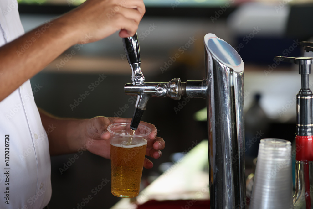 Bartender pours cold beer from the machine into glass.