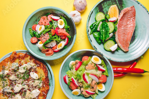 Salad with spinach, eggs and radish in a bowl over bright yellow background. Fish fillet steak, potato and cheese pizza.