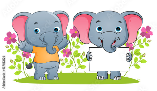 The happy elephant is holding a blank banner and giving the support in the garden