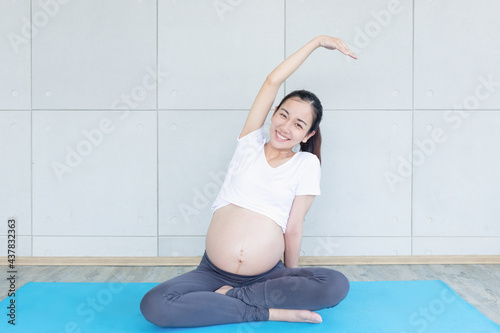 Lady future mother sitting on yoga mat in living room. Pregnant woman doing morning exercises at home.