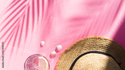 tropical vacation composition - straw hat, water glass and shells on pink background flat lay