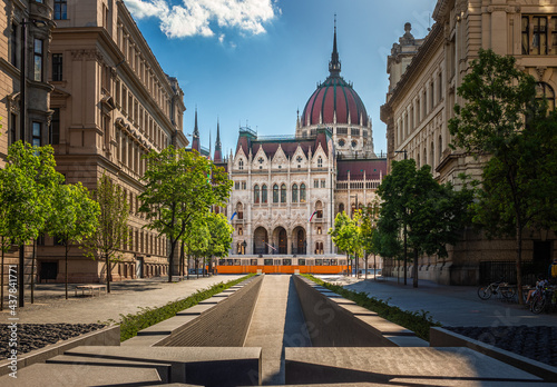 Budapest, Hungary - The Memorial of National Unity in Alkotmany street and Parliament of Hungary with traditional yellow tram on a sunny summer day with blue sky and clouds photo