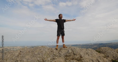 Giovane ragazzo urla a braccia aperte in cima ad una montagna photo