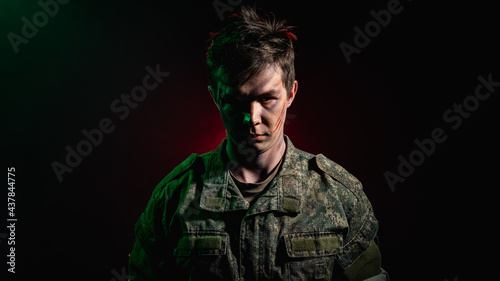 A close-up portrait of a soldier in scars and battle paint, illuminated by green light against a backdrop of red smoke