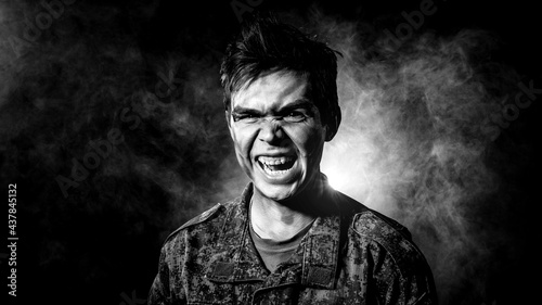 A soldier in military uniform, combat coloring, with scars and bruises screams against the background of smoke, consecrated by a bright spotlight with a black background. Black white contrast portrait