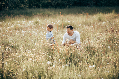 Young dad spends time with his little son in nature, collecting bouquet for mom from wildflowers, single father