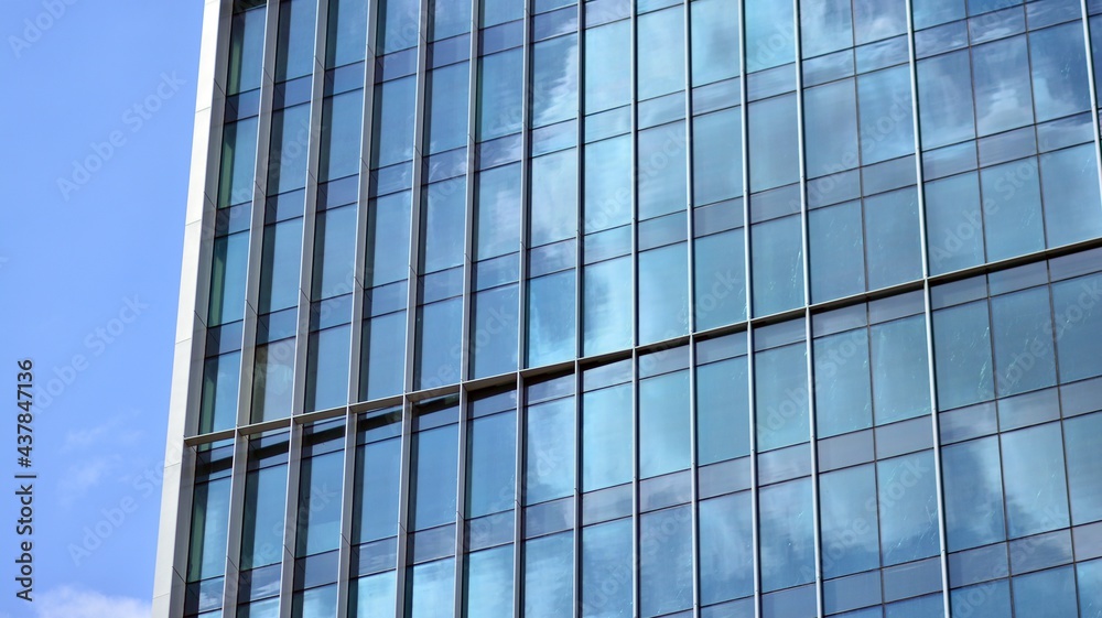 Abstract closeup of the glass-clad facade of a modern building covered in reflective plate glass. Architecture abstract background. Glass wall and facade detail.