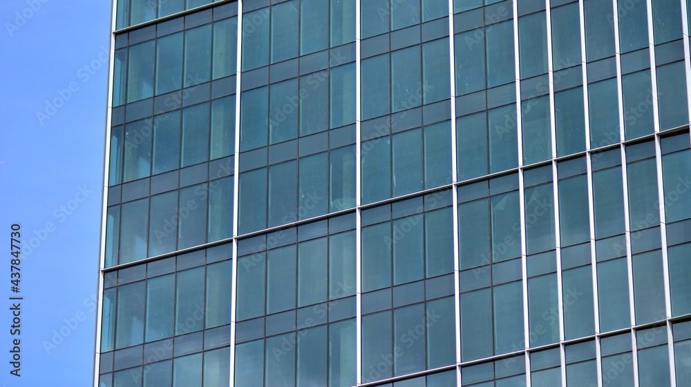 Abstract closeup of the glass-clad facade of a modern building covered in reflective plate glass. Architecture abstract background. Glass wall and facade detail. Abstract closeup of the glass-clad facade of a modern building covered in reflective plate glass. Architecture abstract background. Glass wall and facade detail.