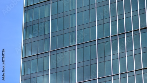 Abstract closeup of the glass-clad facade of a modern building covered in reflective plate glass. Architecture abstract background. Glass wall and facade detail.