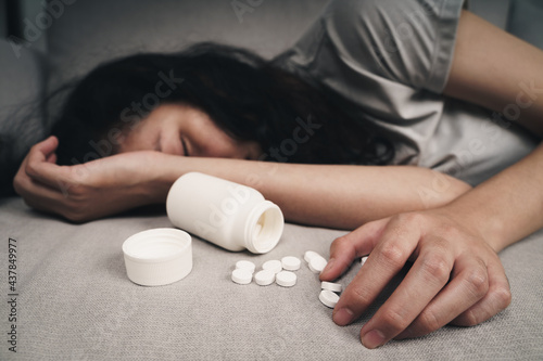 Woman taking medicine overdose and lying on the couch with open pills bottle. overdose and suicide Concept.