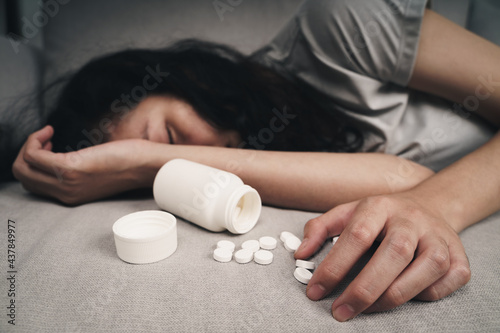 Woman taking medicine overdose and lying on the couch with open pills bottle. overdose and suicide Concept. photo