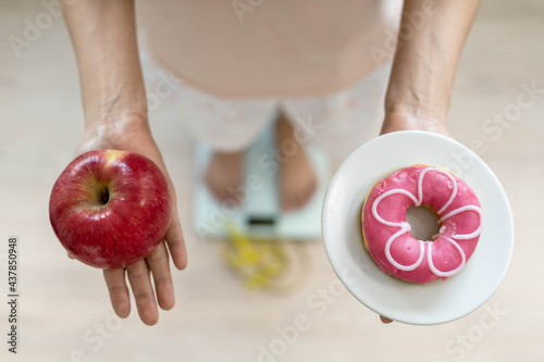 Women are choosing the right food for good health. Women are fasting. Comparison options between donuts and apples during weight measurement on digital scales. Diet concept.