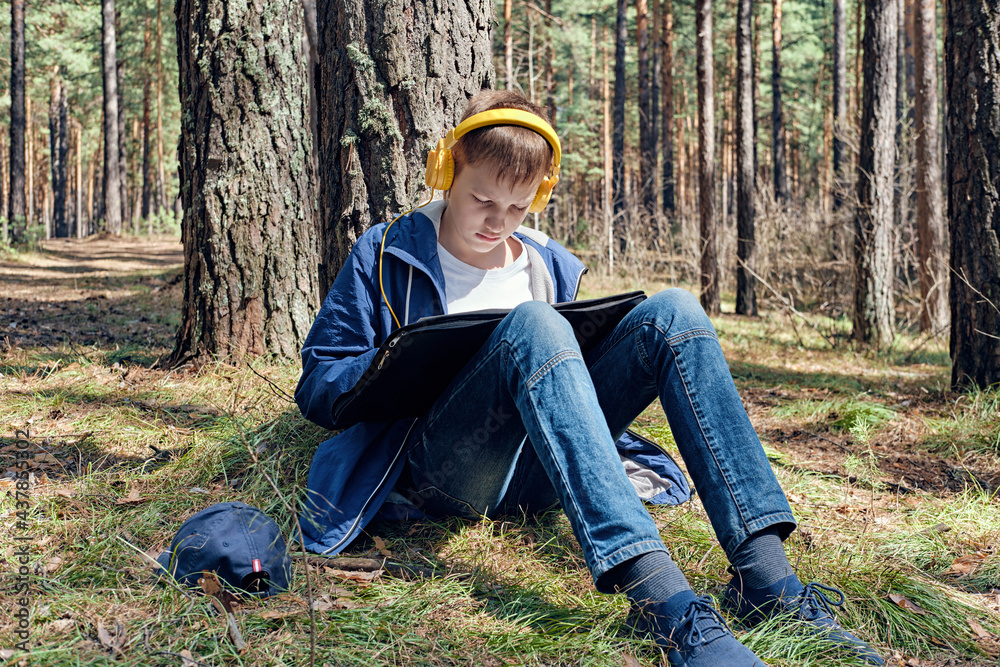 Young artist sits in pine forest and plein air painting and listens to music. Sunny day, creative leisure Young artist sits in pine forest and plein air painting and listens to music. Sunny day, creative leisure