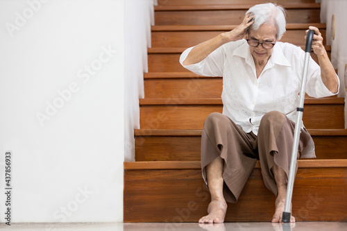 Asian senior woman have a severe headache,disease of brain tumor or brain cancer,pain in her head,sick old elderly sits on the floor of the stairs to rest her vertigo,dizzy,tendency to fall or stagger