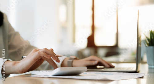 Close up hand of businesswoman making calculation with calculator and laptop computer at modern office photo