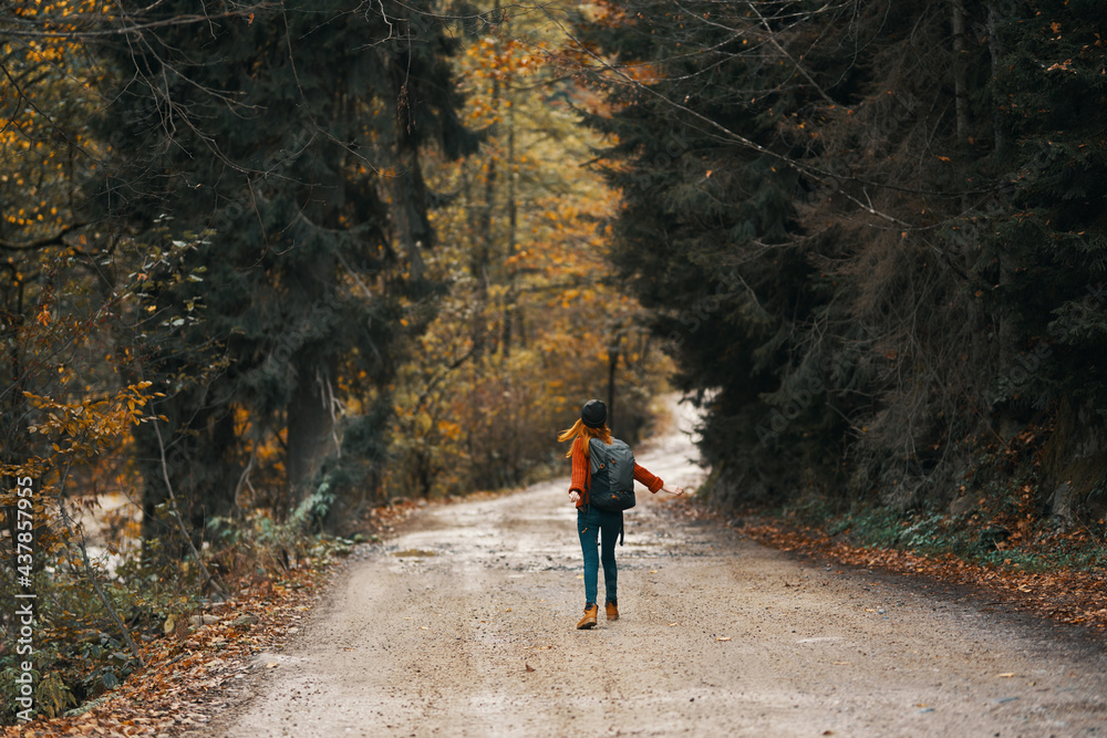 happy travel with a backpack in a warm sweater, trousers and boots walks along the road in the autumn forest