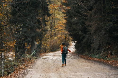 happy travel with a backpack in a warm sweater, trousers and boots walks along the road in the autumn forest
