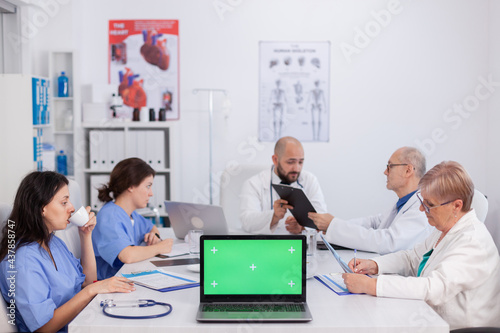 Mock up green screen chroma key laptop computer with isolated display standing on desk in conference meeting room. Doctors teamwork discussing microbiology expertise analyzing disease research
