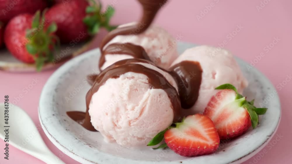 Pouring chocolate sauce on strawberry ice cream. Pink strawberry ice cream scoops served with chocolate topping