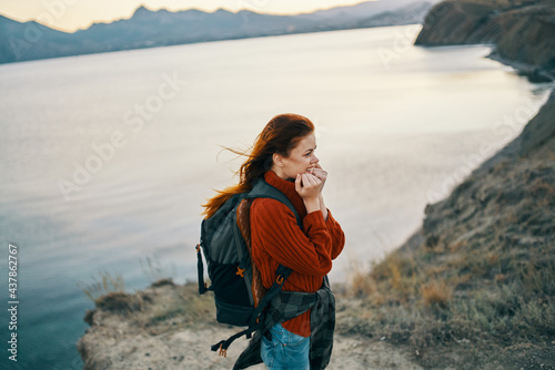hiker with a backpack in the mountains near the sea and a red sweater loose hair sunset rocks