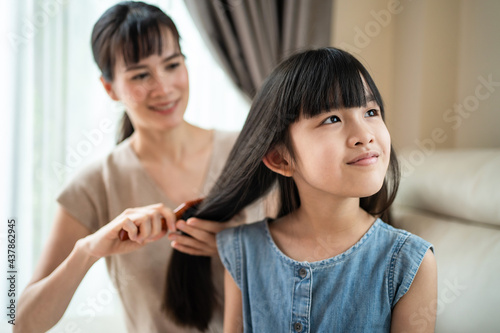 Parent mom comb little girl child's hair with hairbrush in living room