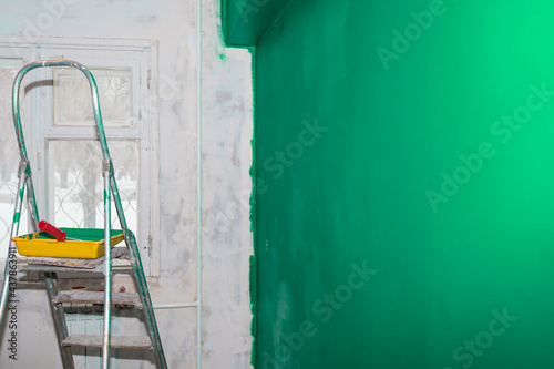 Stepladder, paint tray and roller on the background of a green wall. Copy space