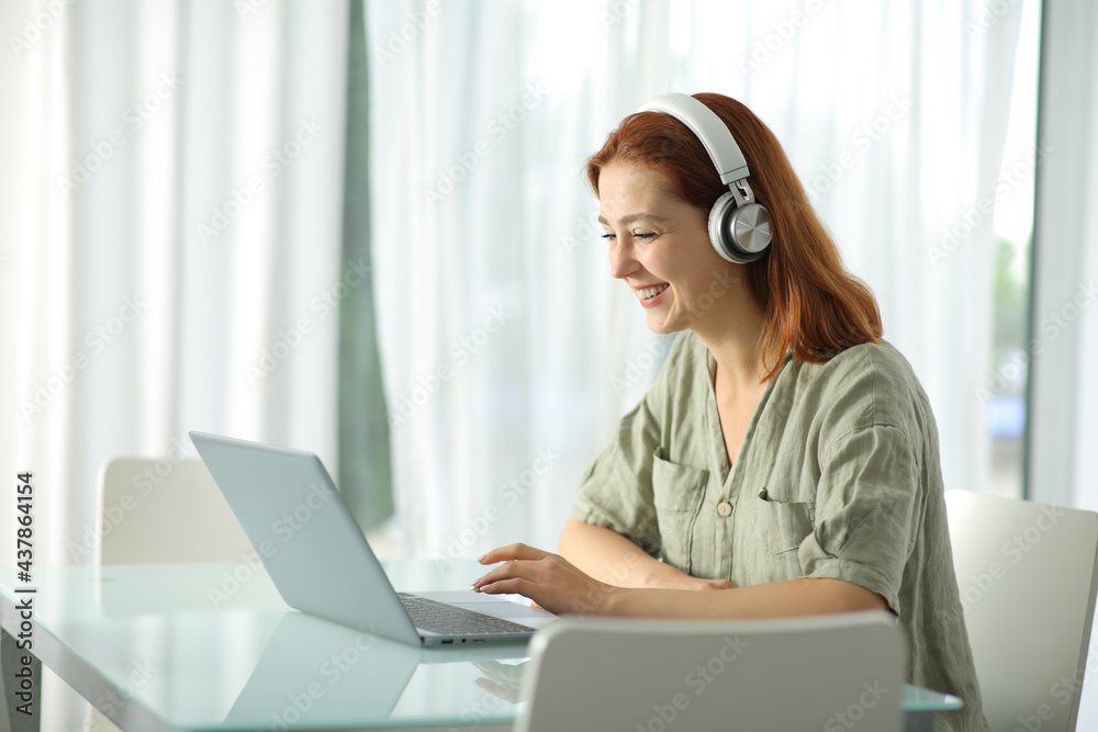 Happy woman with headphones checking laptop at home Happy woman with headphones checking laptop at home