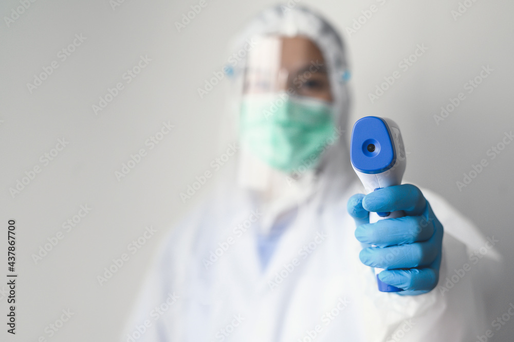 Close up shot of doctor wearing protective face mask and PPE suit using infrared forehead thermometer to check body temperature Close up shot of doctor wearing protective face mask and PPE suit using infrared forehead thermometer to check body temperature