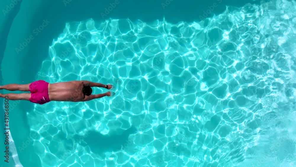Top down slow motion view of a man diving into the fresh pool water during a hot summer day